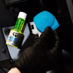 Dacia Duster: ręka w czarnej rękawiczce trzyma niebieską zakrętkę od wlewu płynu do spryskiwaczy i buteleczkę koncentratu K2 Nuta Max.