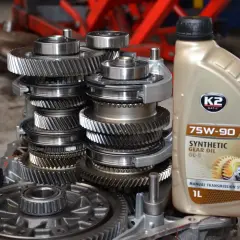 Jaki olej do skrzyni biegów? Butelka oleju syntetycznego 75W-90 GL-5 obok mechanizmu zębatek.