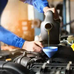 Mechanik w niebieskim kombinezonie wykonuje wymianę oleju w samochodzie, nalewając płyn do silnika przez lejek.