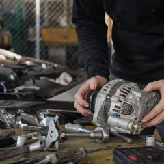 Mechanik trzyma alternator, zastanawiając się, ile trwa regeneracja alternatora. Na stole leżą narzędzia.