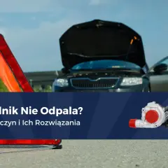 Rozładowany akumulator po dłuższym postoju? Awaryjny trójkąt i otwarty bagażnik czarnego auta sugerują problem z odpaleniem silnika.