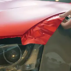 Przemalowanie samochodu na jaskrawy czerwony. Ręka delikatnie naciąga folię na błotnik.