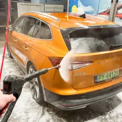 Jak dobrze umyć auto na myjni bezdotykowej? Pomarańczowa Skoda Enyaq jest spryskiwana wodą pod ciśnieniem.