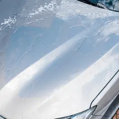 Krople wody spływają po masce srebrnego auta, tworząc smugi. Czy po woskowaniu płukać auto? Tak, aby uzyskać idealny połysk.