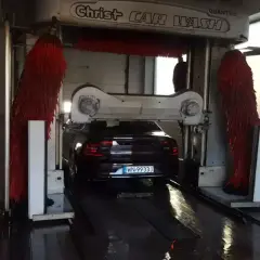 Ciemny Volvo czeka na mycie auta w automatycznej myjni. Czerwone szczotki są gotowe do pracy.