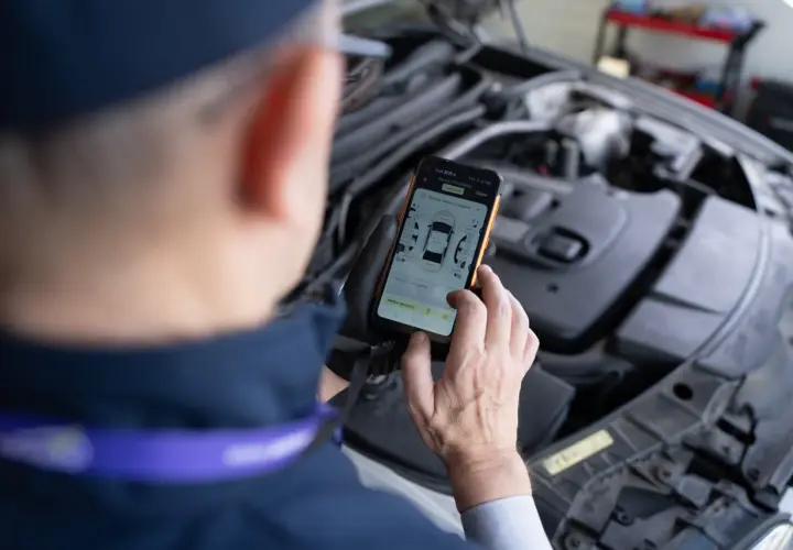 Mechanik sprawdza na telefonie raport z pomiaru lakieru i szczelin, szukając informacji o kodach błędów DTC.