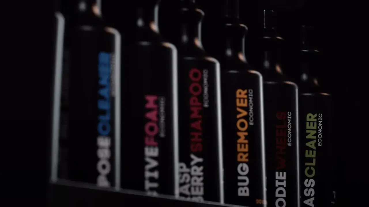 Rząd czarnych butelek z etykietami: "POSECLEANER", "CTIVEFOAM", "RASPBERRY SHAMPOO", "BUGREMOVER", "ODIE WHEELS", "ASSCLEANER". To są kosmetyki do samochodu.