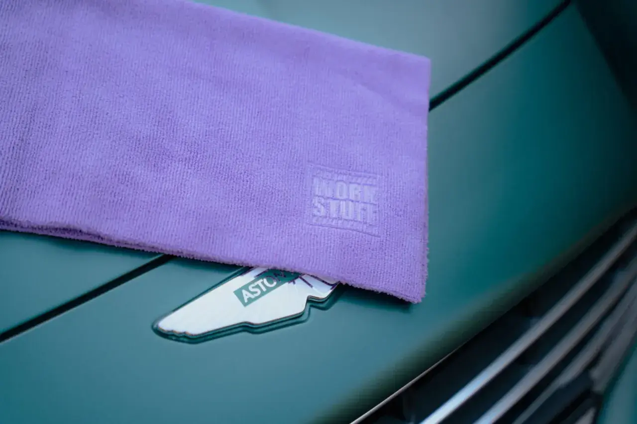 Fioletowy ręcznik z mikrofibry z logo Work Stuff leży na zielonym samochodzie Aston Martin. Dowiedz się, jak prać ręcznik z mikrofibry, by służył latami.