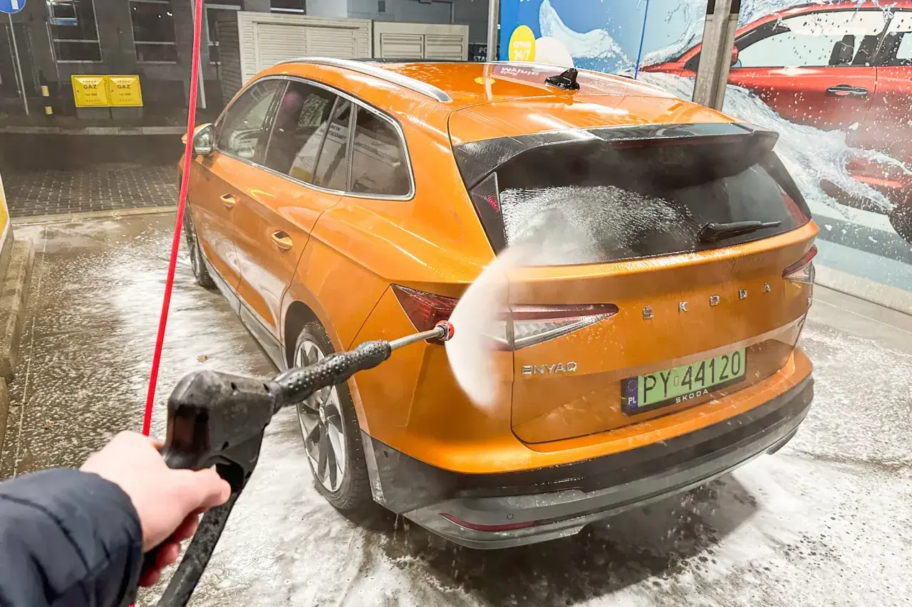 Jak dobrze umyć auto na myjni bezdotykowej? Pomarańczowa Skoda Enyaq jest spryskiwana wodą pod ciśnieniem.