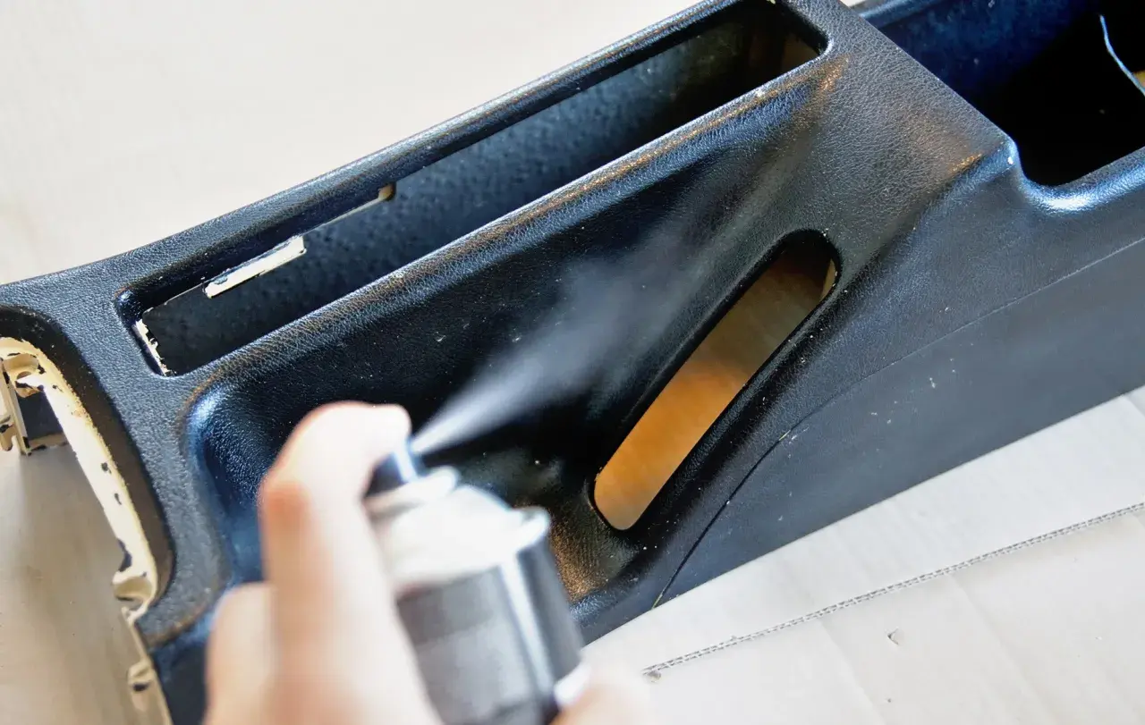 Ręka trzyma puszkę z farbą w sprayu, wykonując malowanie plastików. Odświeżanie wnętrza samochodu.
