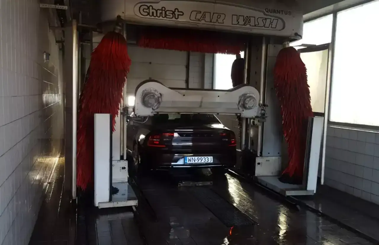 Ciemny Volvo czeka na mycie auta w automatycznej myjni. Czerwone szczotki są gotowe do pracy.