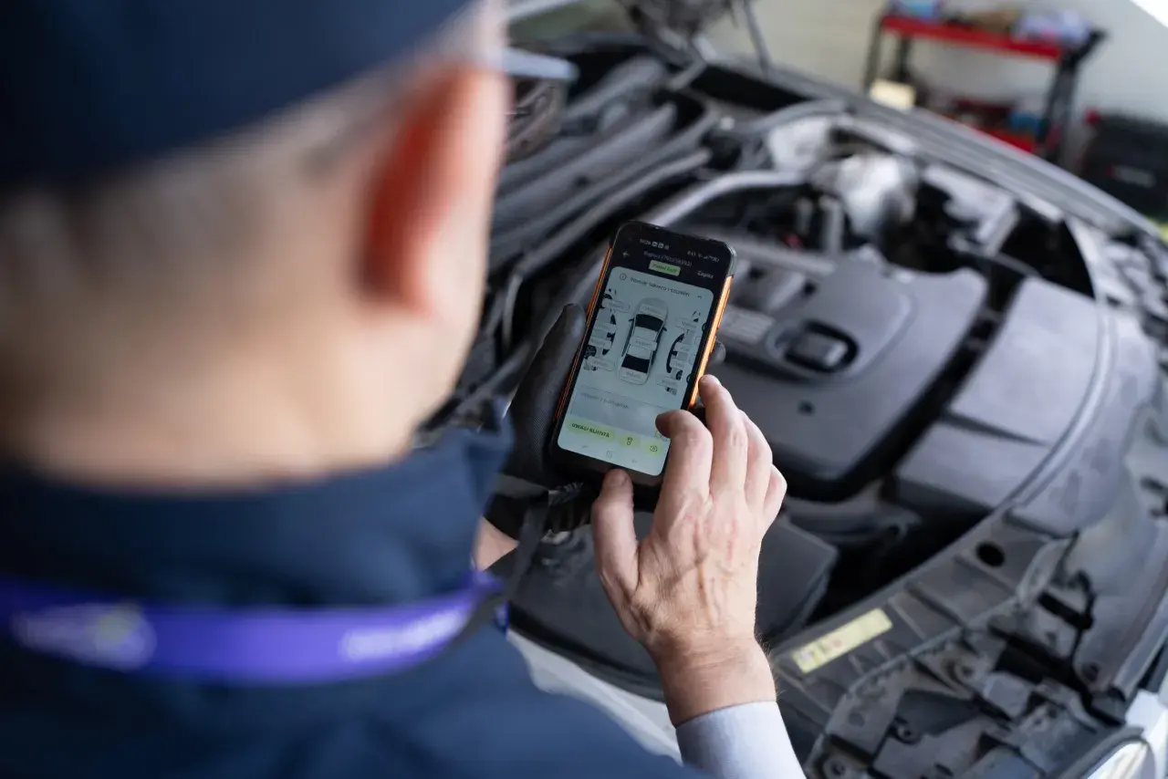 Mechanik sprawdza na telefonie raport z pomiaru lakieru i szczelin, szukając informacji o kodach błędów DTC.