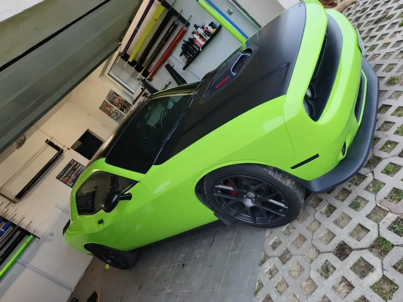 Jasnozielony Dodge Challenger po oklejaniu folią, z czarną maską i dachem. W tle rolki folii i akcesoria do oklejania.