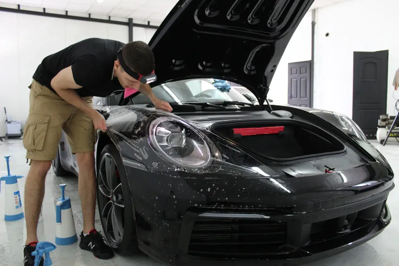 Mężczyzna aplikuje folia ppf na auto, chroniąc lak czarnego Porsche.