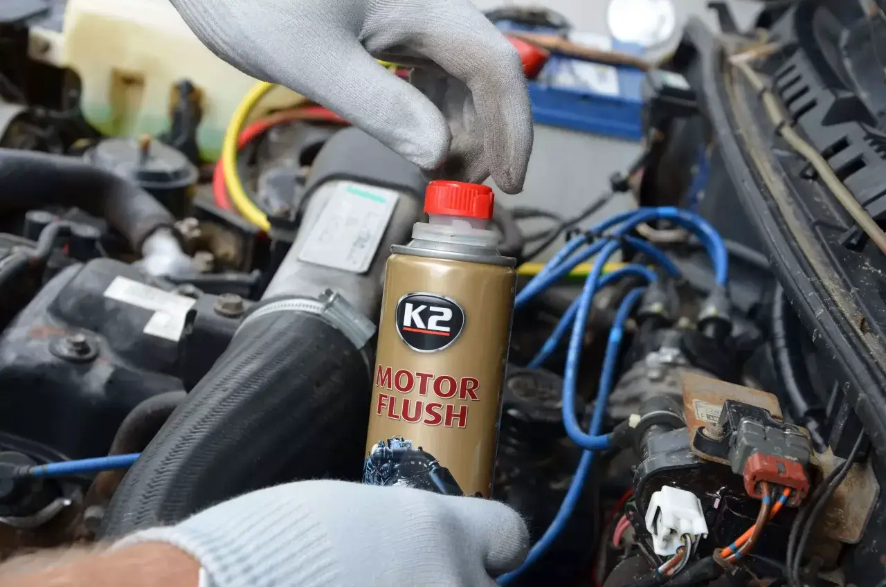 Ręka w rękawiczce trzyma puszkę K2 Motor Flush, gotową do użycia w silniku samochodu.