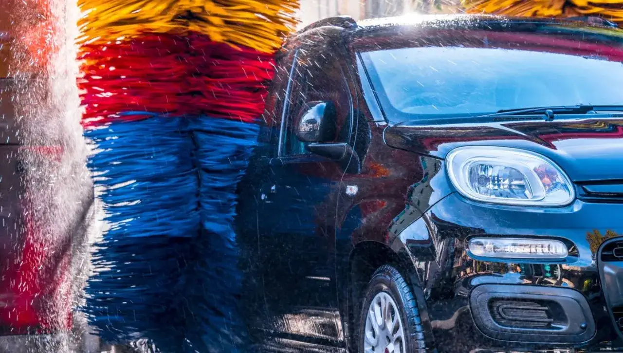 Czarna karoseria lśni w myjni automatycznej, a kolorowe szczotki obracają się, budząc wątpliwości, czy myjnia automatyczna niszczy lakier.